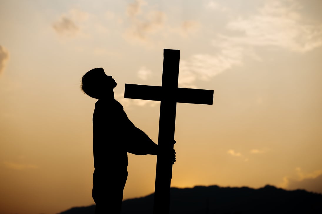 Silhouette of a man praying before a cross at sunset. concep